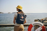 a girl wearing fjallraven cap and carrying a kanken totepack enjoying the view of lake 