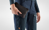 someone is standing with wearing fjallraven dark navy branded durable trouser and a pouch in his hand.