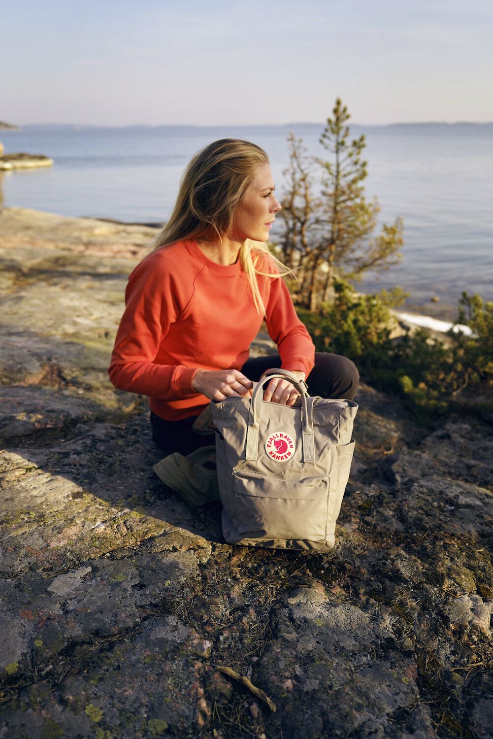 a girl wearing fjallraven cap and carrying a Kånken totepack enjoying the view of lake 