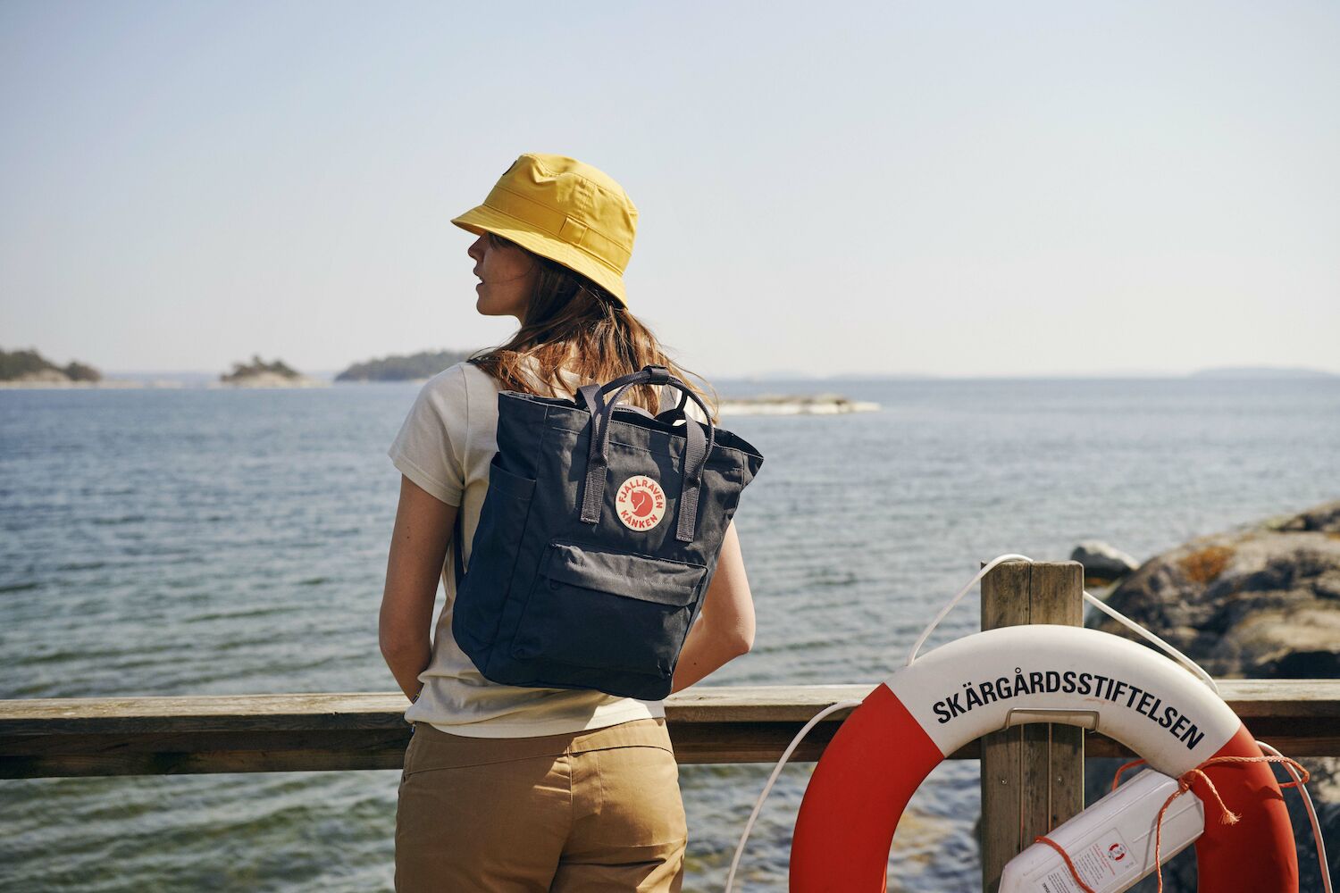 a girl wearing fjallraven cap and carrying a kanken totepack enjoying the view of lake 