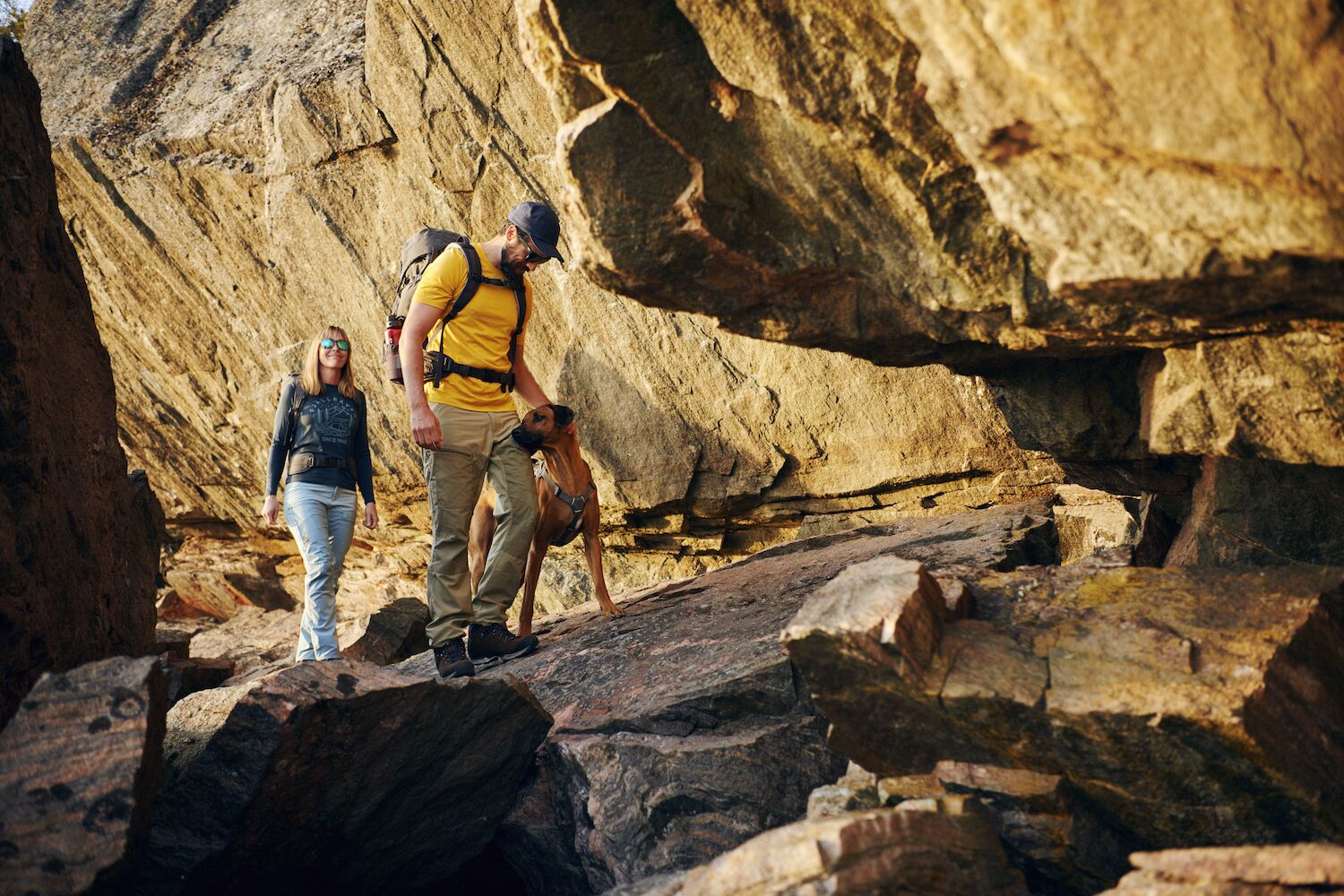 one man is trekking in the rocks with his wife and his pet dog wearing branded fjallraven clothing.